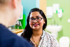 A close up over the shoulder photo of a female wearing glasses smiling at the person she is talking to.